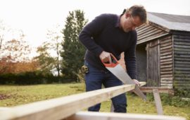 Man Sawing Wood next to Garden Shed