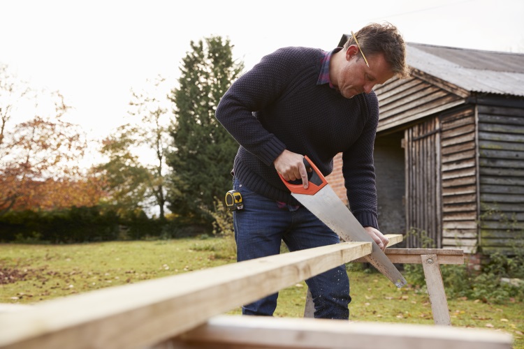 Man Sawing Wood next to Garden Shed