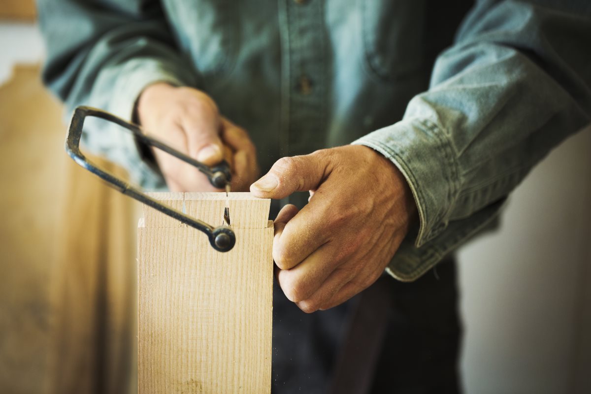 A man using a handsaw on a piece of wood. Garden Power Tools